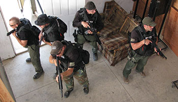 Two officers with shotguns take point while team members with high-capacity automatic pistols and an officer with a tactical rifle are ready to provide suppressive fire during this room-clearing exercise.